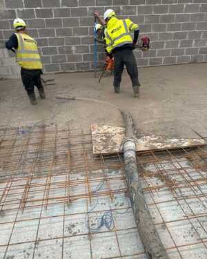 Construction workers in safety gear working on a concrete floor with a wall in the background.