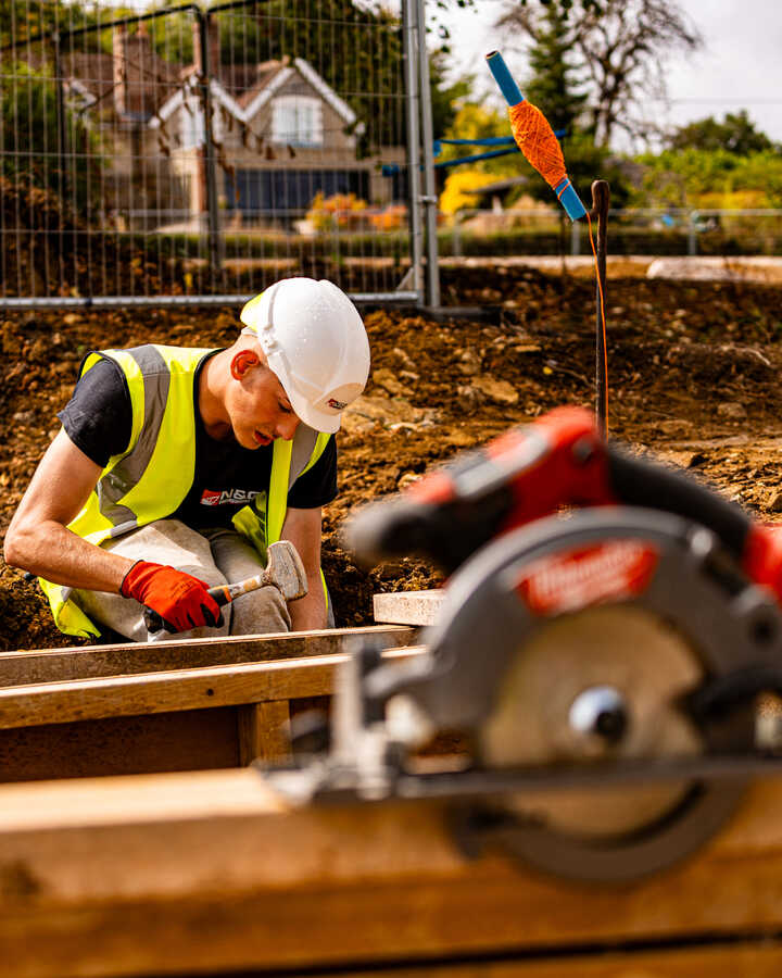 Construction site with foundations and materials laid out on gravel under a clear blue sky.