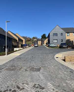 A quiet cobblestone street lined with modern houses under a clear blue sky.