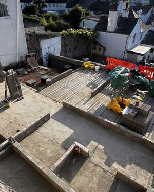 Construction site with concrete foundations, machinery, and surrounding buildings.