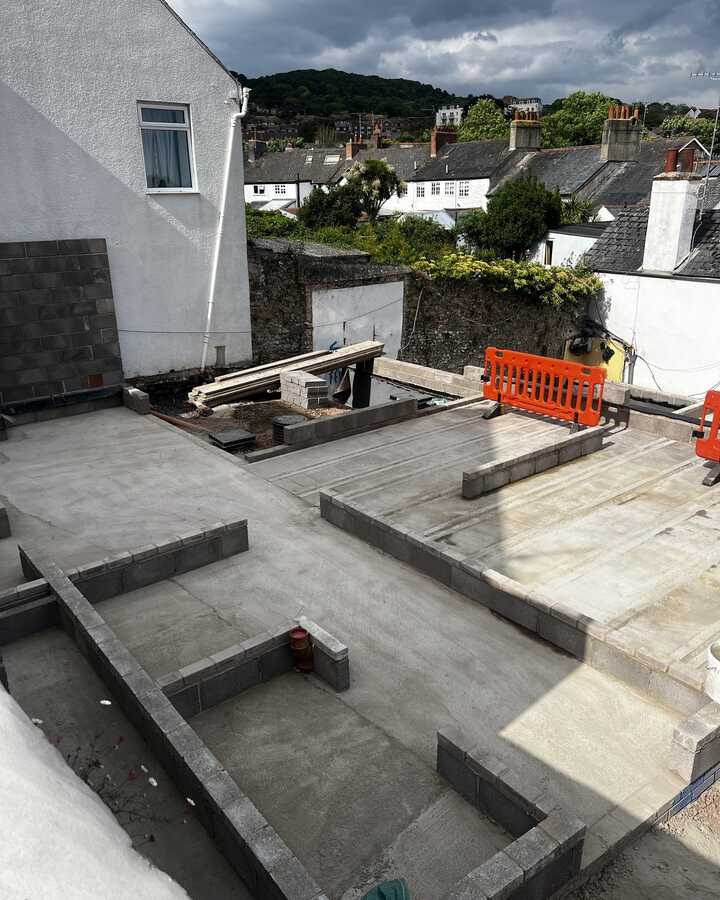 Construction site with a concrete foundation and building materials; cloudy sky above.