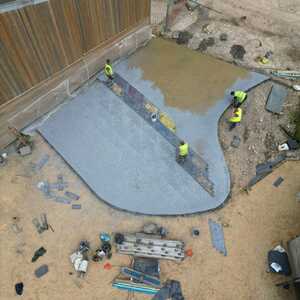 Construction workers pouring concrete for a foundation near a building.