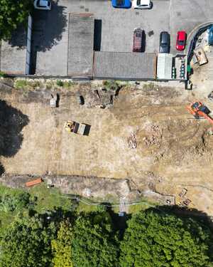 Aerial view of a cleared construction site with parked cars and surrounding greenery.