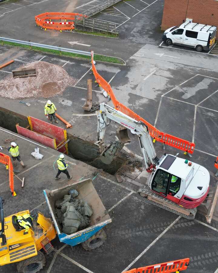 Construction site with workers, machinery, and barriers in a parking lot.