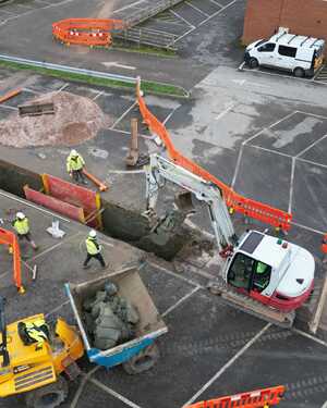 Construction site with workers, machinery, and barriers in a parking lot.