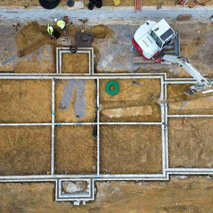 Construction site with foundation outlines and an excavator in a dirt area.