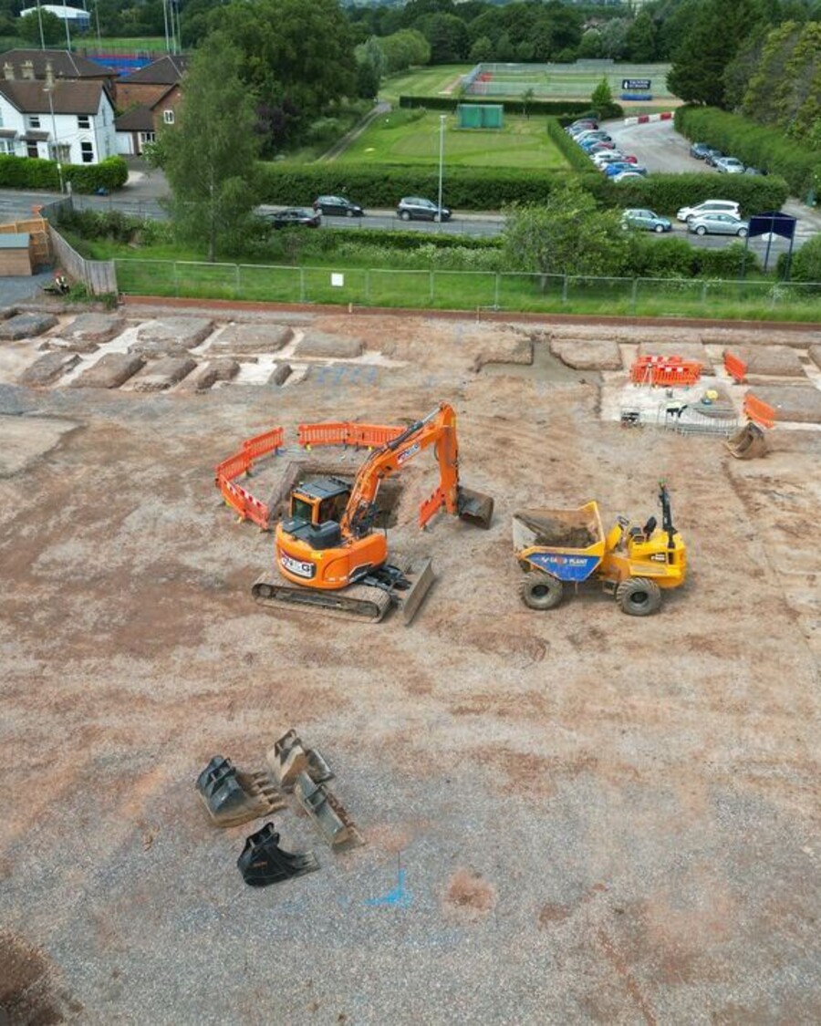 Construction site with machinery, marked areas, and a worker in a yellow vest.
