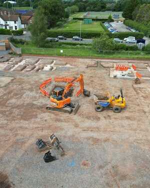 Construction site with machinery, marked areas, and a worker in a yellow vest.
