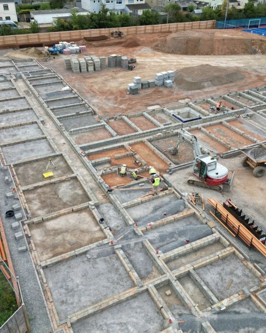 Construction site with foundations laid, machinery, and materials visible.