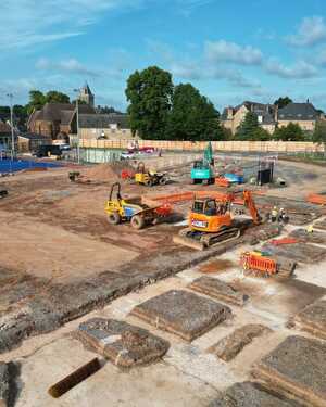 Construction site with an excavator, dumper truck, and a worker in a safety vest.