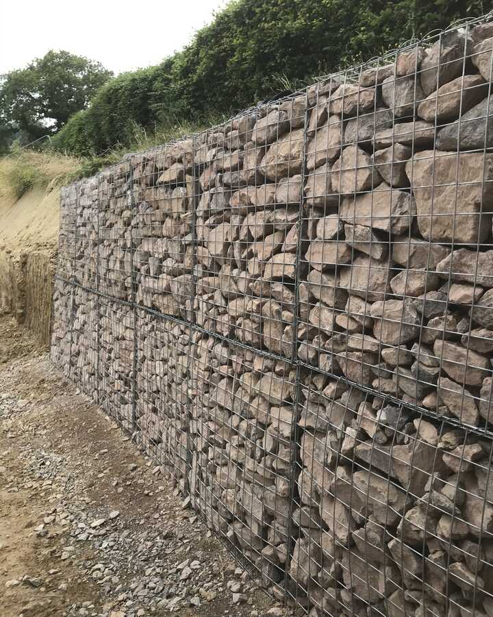 Gabion wall made of stacked stones in a wire mesh structure.