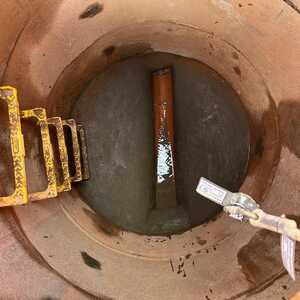View into a sewer with a metal ladder and sewer pipe visible at the bottom.