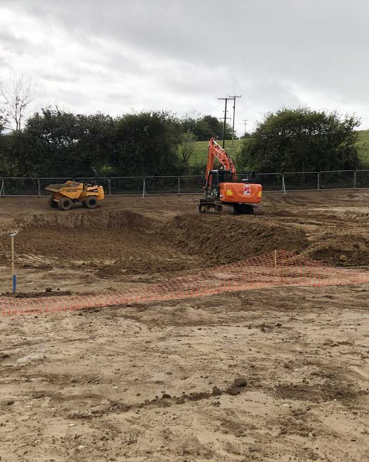 Construction site with excavators and workers in a cleared area under a cloudy sky.