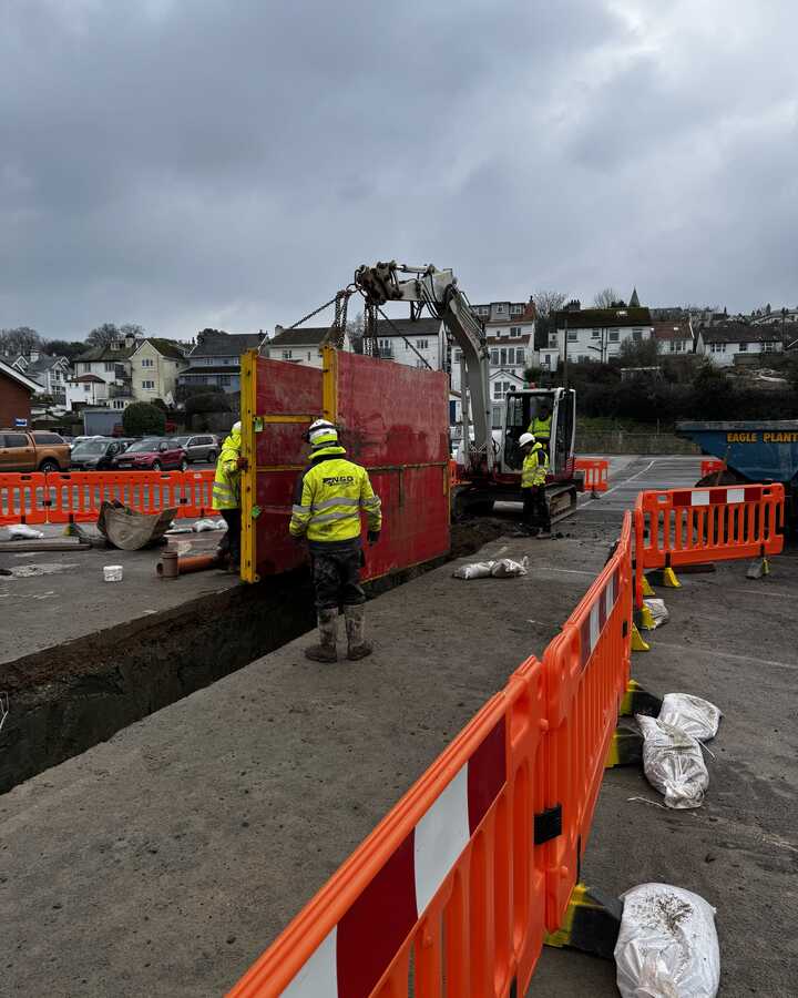 Construction workers moving a large red wall panel with machinery at a worksite.