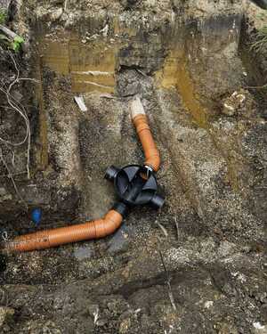 Excavated ground with orange drainage pipes and a black connector visible.