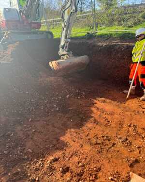 Excavator digging a trench with a worker observing nearby.