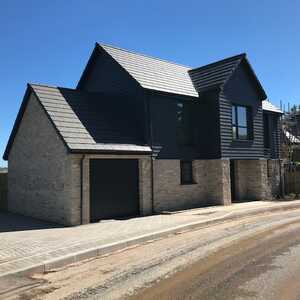 Modern two-story house with a mix of stone and dark siding set against a clear blue sky.