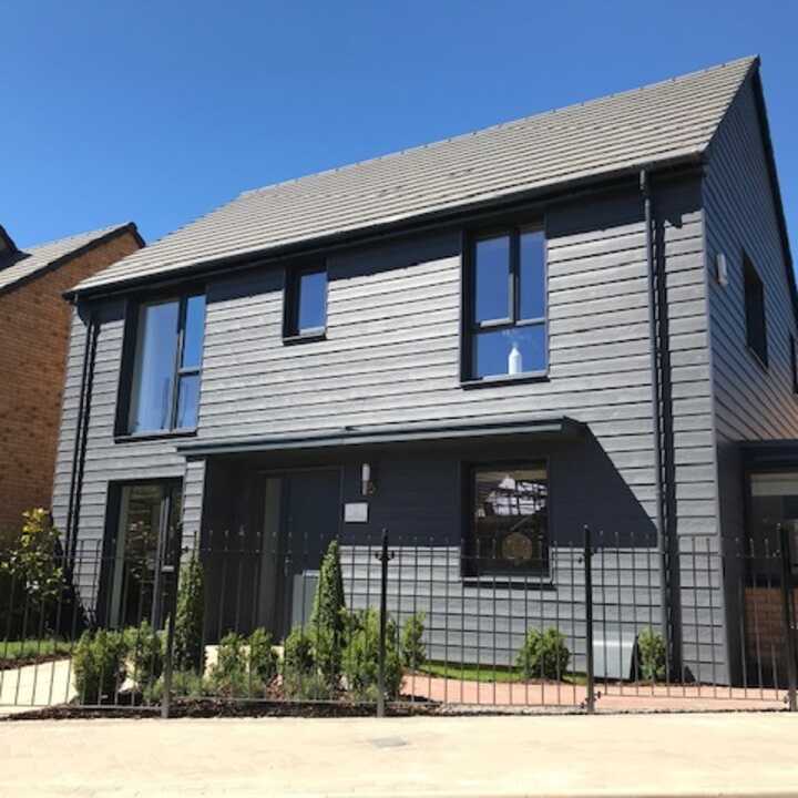 Modern two-story house with a gray exterior and blue accents, surrounded by a fence.