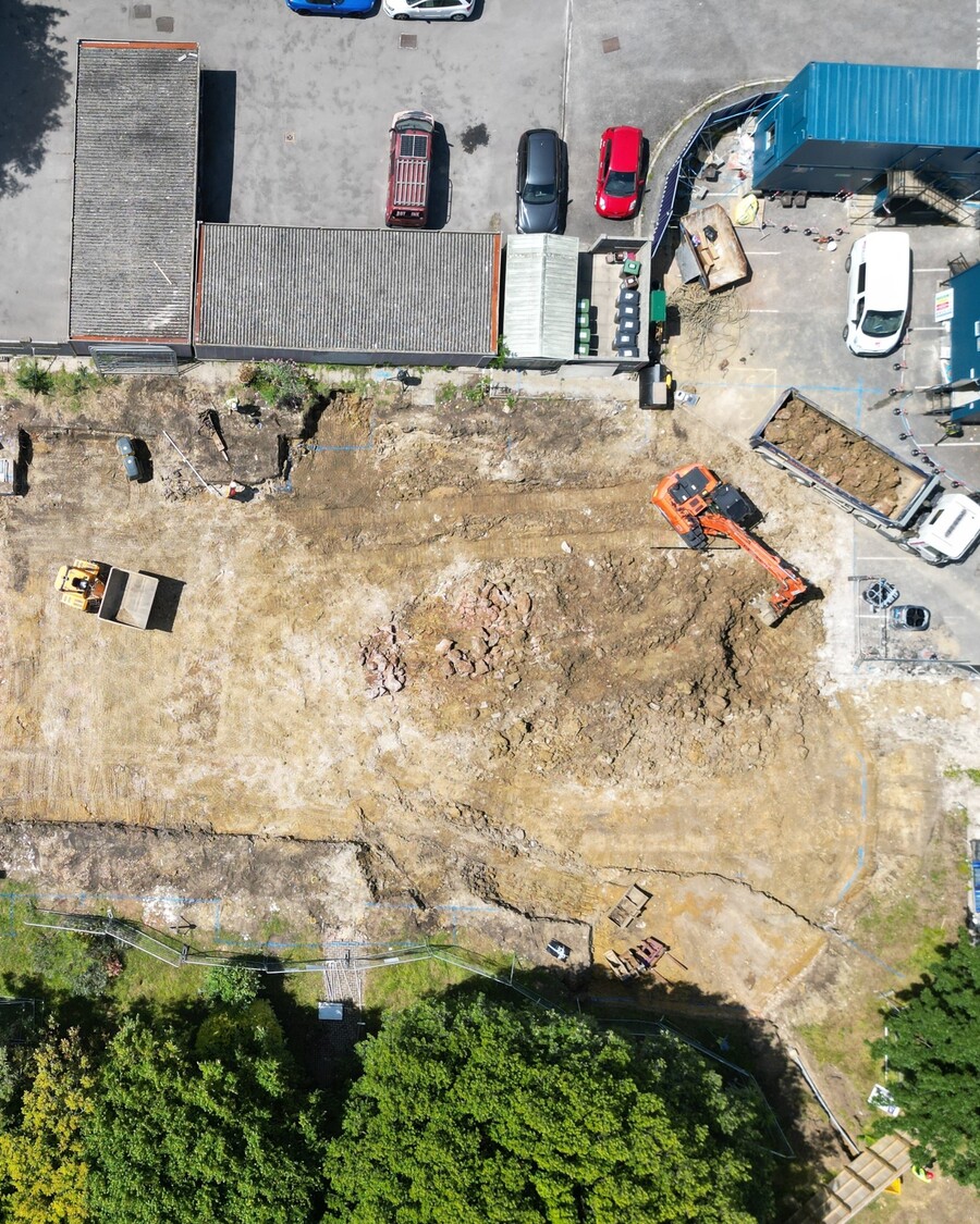 Aerial view of a construction site with machinery, dirt, and parked cars.