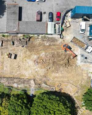 Aerial view of a construction site with machinery, dirt, and parked cars.